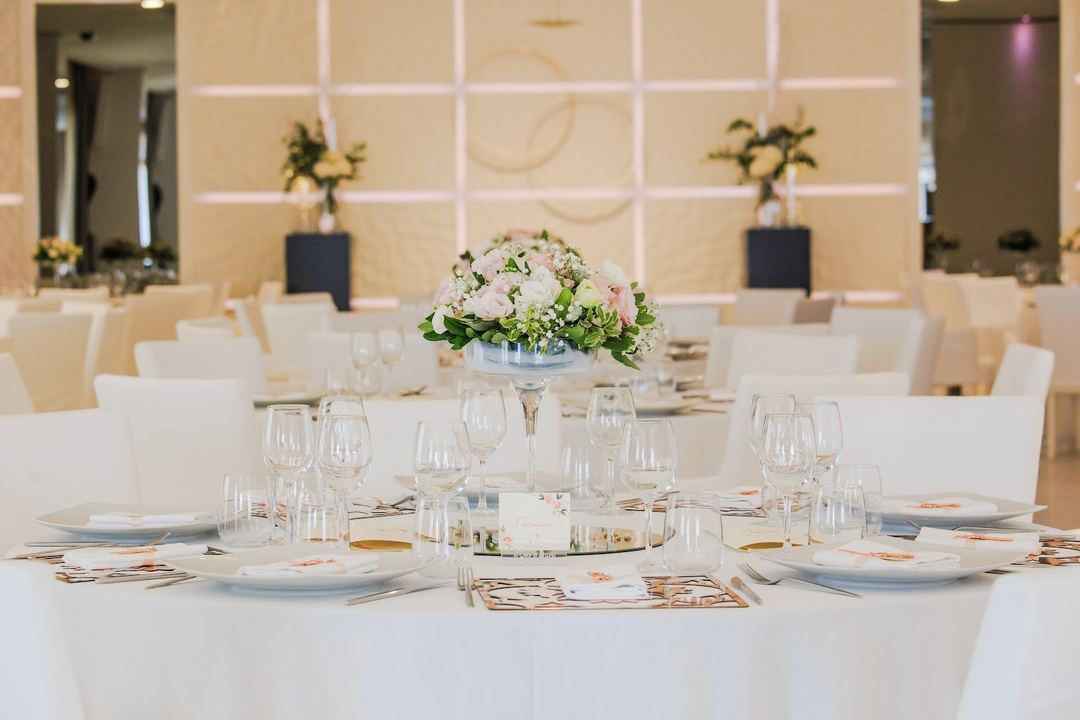 An elegantly set banquet table with white linens, crystal glassware, and a floral centerpiece in a sophisticated event space.